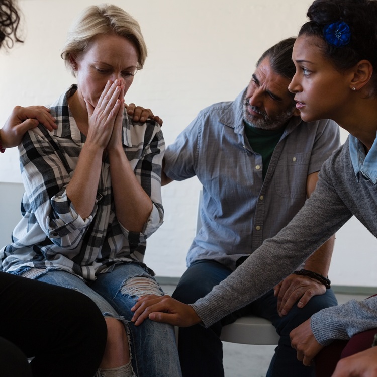 Friends Consoling Worried Female While Sitting On Chair In Art Class